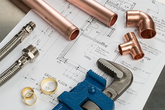 Plumbing supplies and tools - copper pipes, fittings, and wrench on blueprints