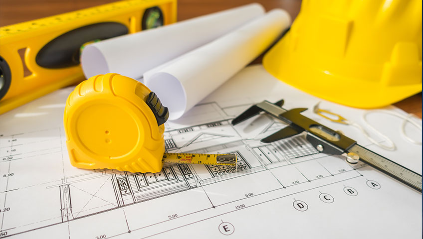 Construction planning tools - yellow measuring tape, hard hat, and blueprints with architectural drawings